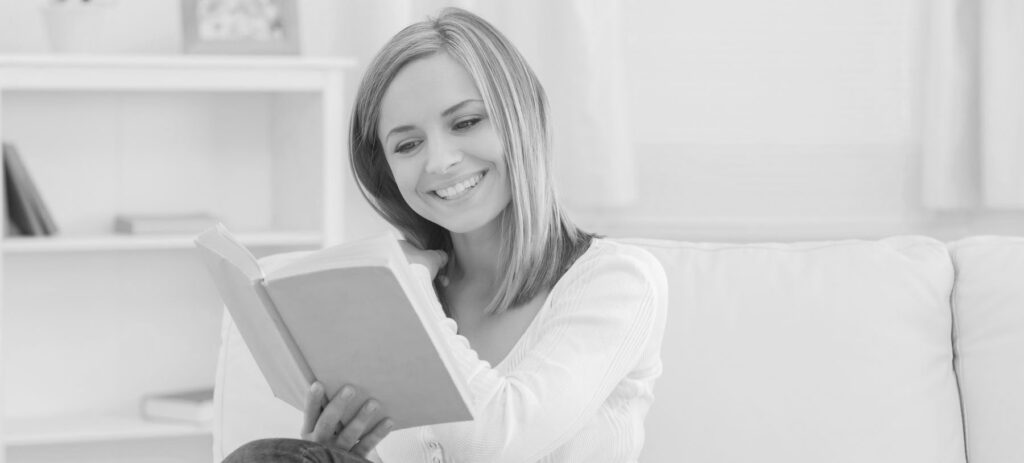 Happy young woman reading storybook on couch at home